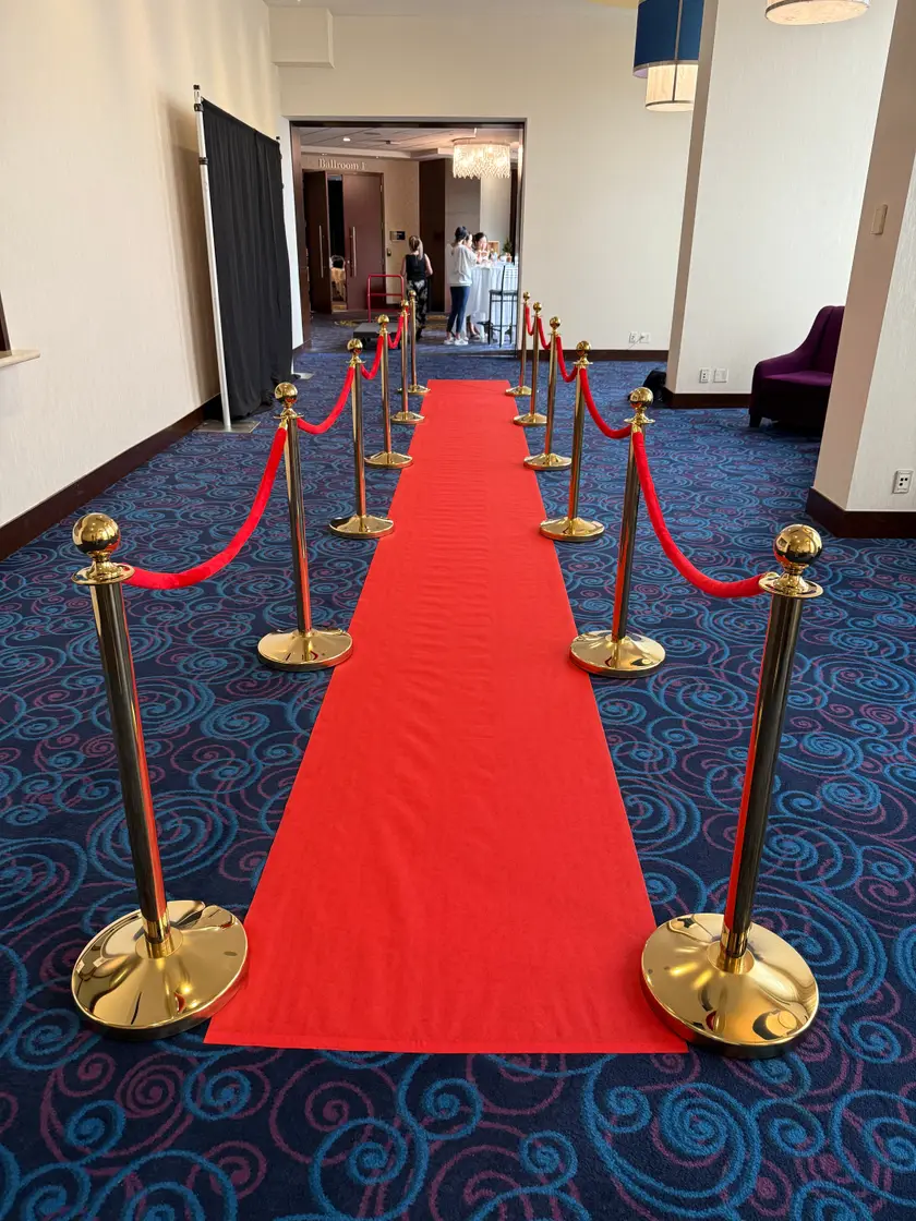 A red carpet runner with gold rope stanchions down both sides in a hotel corridor